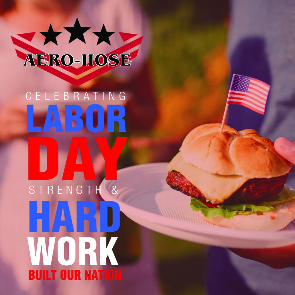 promotional image for auto-hose celebrating labor day, featuring a hand holding a hamburger with a small american flag, with blurry people in the background.