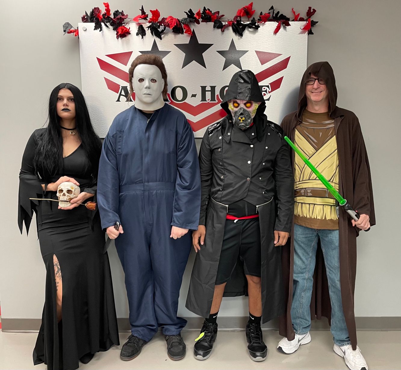 four people in halloween costumes posing in front of an auto draft banner, featuring characters like morticia addams, michael myers, a cyberpunk fighter, and a jedi.