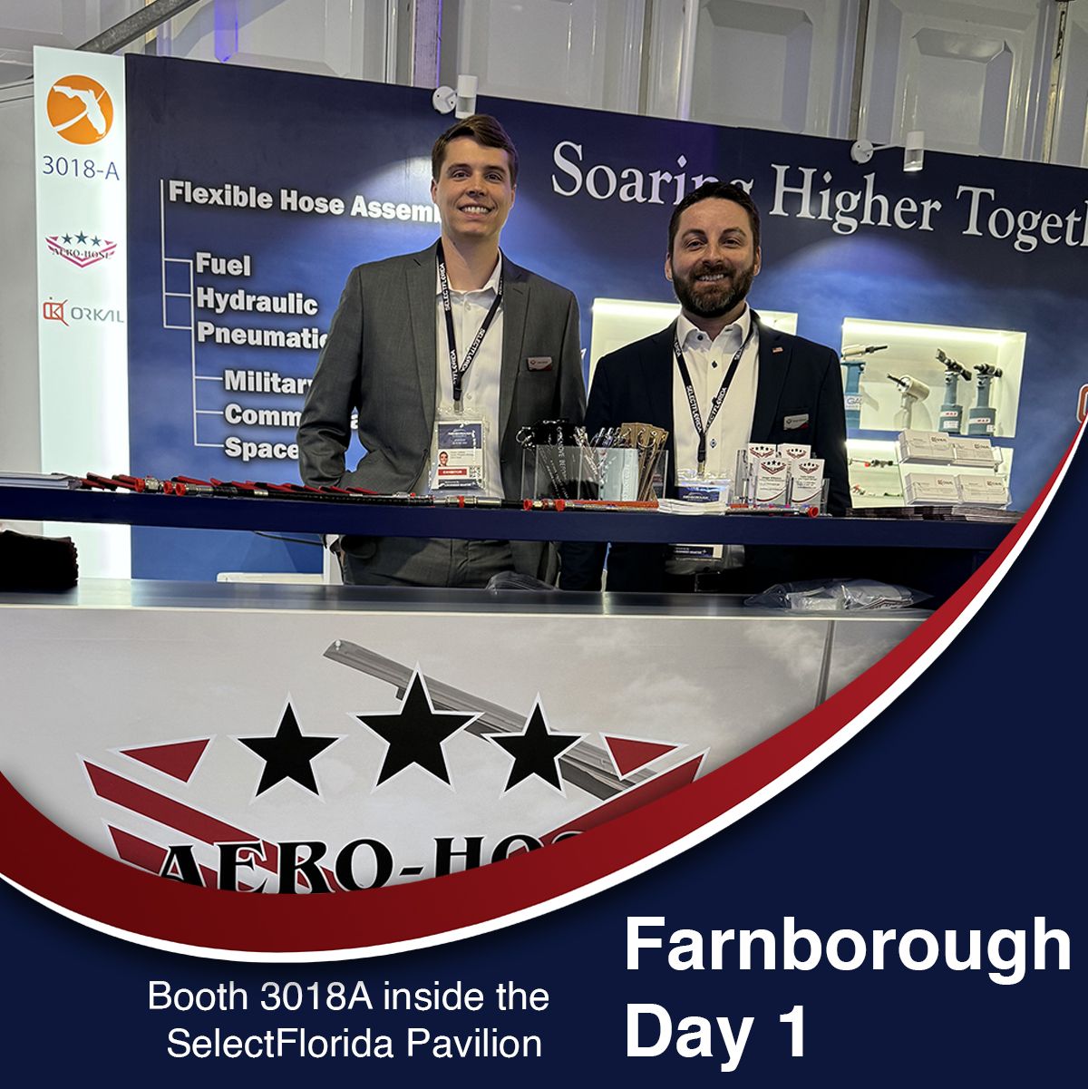 two men standing at a trade show booth for aero-hose at farnborough, with a display showcasing flexible hose assemblies for various applications. text reads: "farnborough day 1. booth 3018a inside the selectflorida pavilion. auto draft solutions also featured.