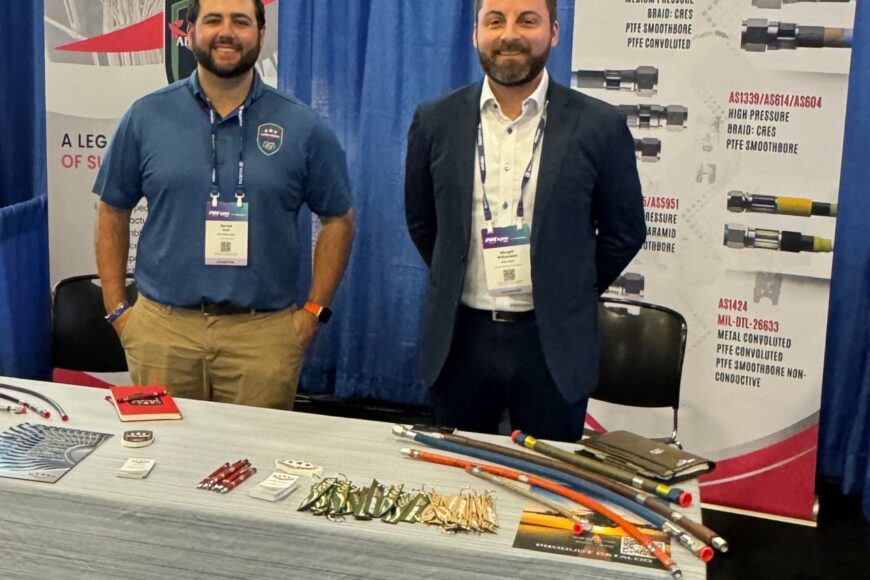 Two people standing behind a trade show booth displaying Aero-Hose products and promotional materials.